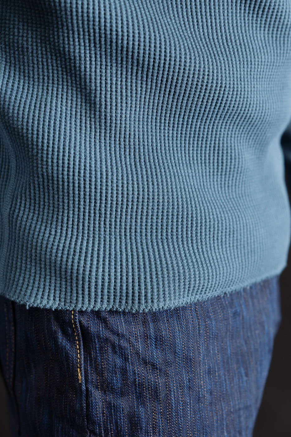 Close-up of front hem and waffle knit texture on blue Studio D'Artisan 9937 heavy thermal long sleeve henley, shown on male model's torso over denim jeans.