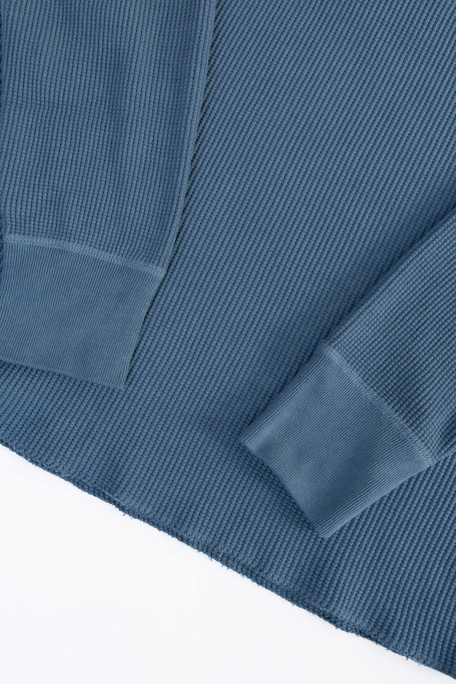 Close-up of Studio D'artisan 9937 Heavy Thermal Henley in blue, showing sleeve cuffs, ribbed texture, and raw hem detail, front view flat lay.