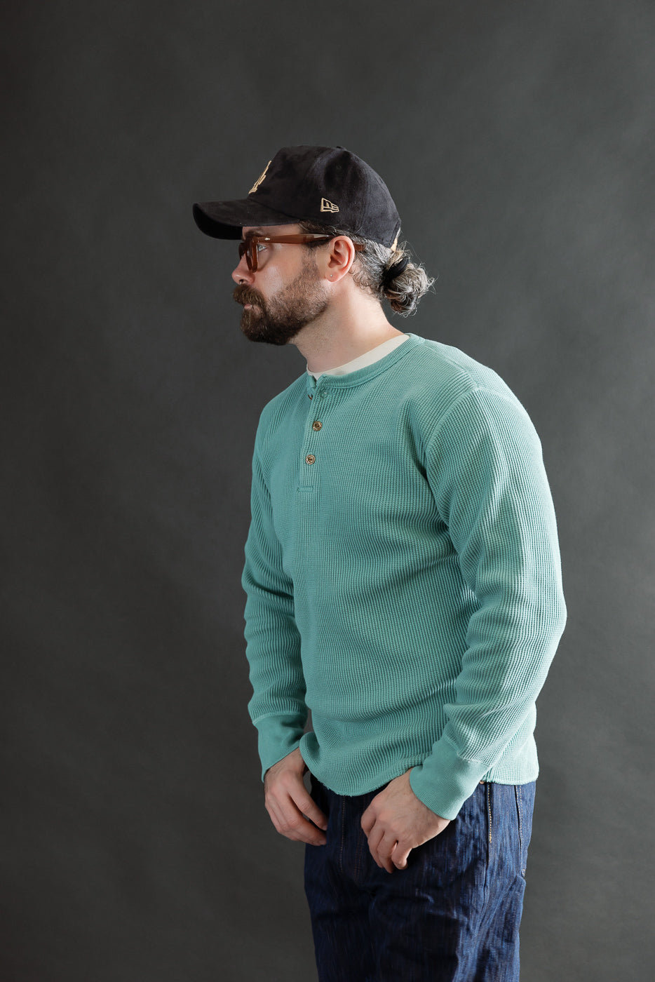 Male model 5'9, 165lbs, athletic build wearing Studio D'Artisan emerald heavy thermal long sleeve henley, side view, showing textured fabric and front button placket.