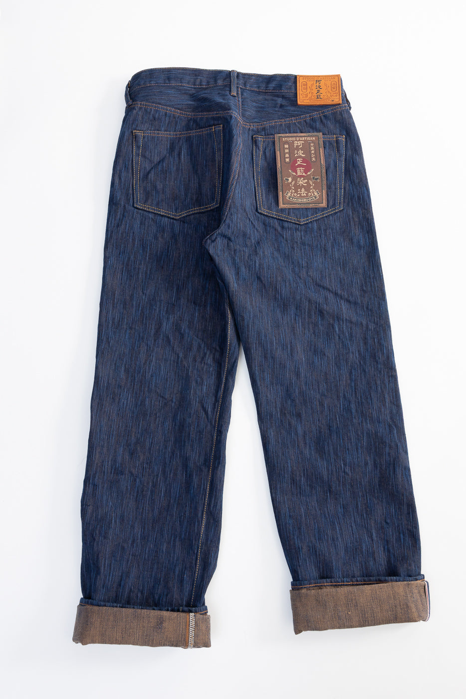 Back view flat lay of Studio D'Artisan 15oz Awa Shoai Kakishibu natural indigo selvedge jeans, showcasing rear pockets, leather patch, and straight leg fit.