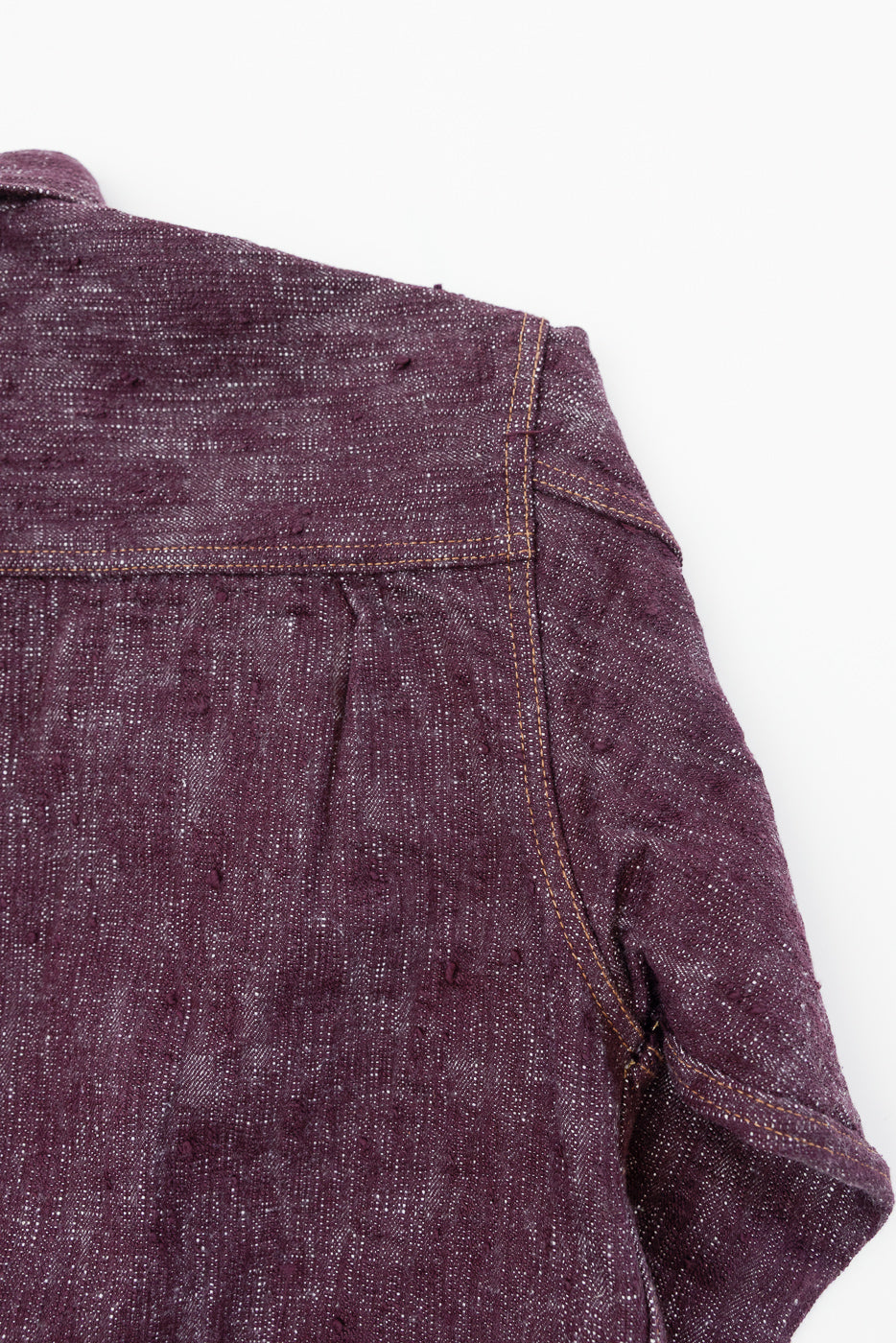 Close-up front shoulder of purple selvedge shirt, showing textured fabric, contrast stitching, and sleeve detail