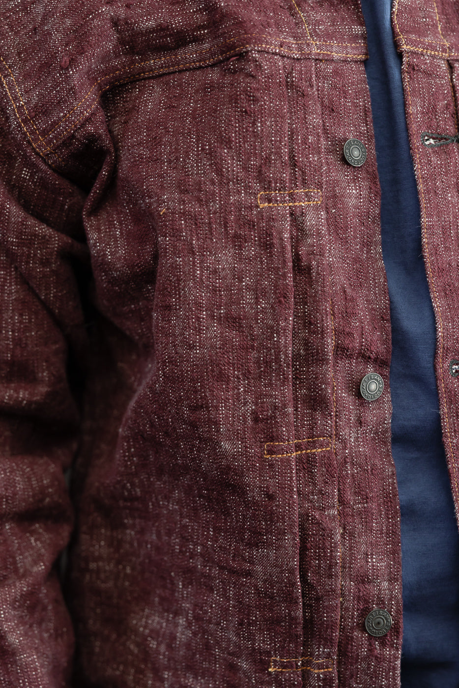 Close-up front view of maroon selvedge shirt jacket, showing button placket, contrast stitching, and textured fabric on male model.