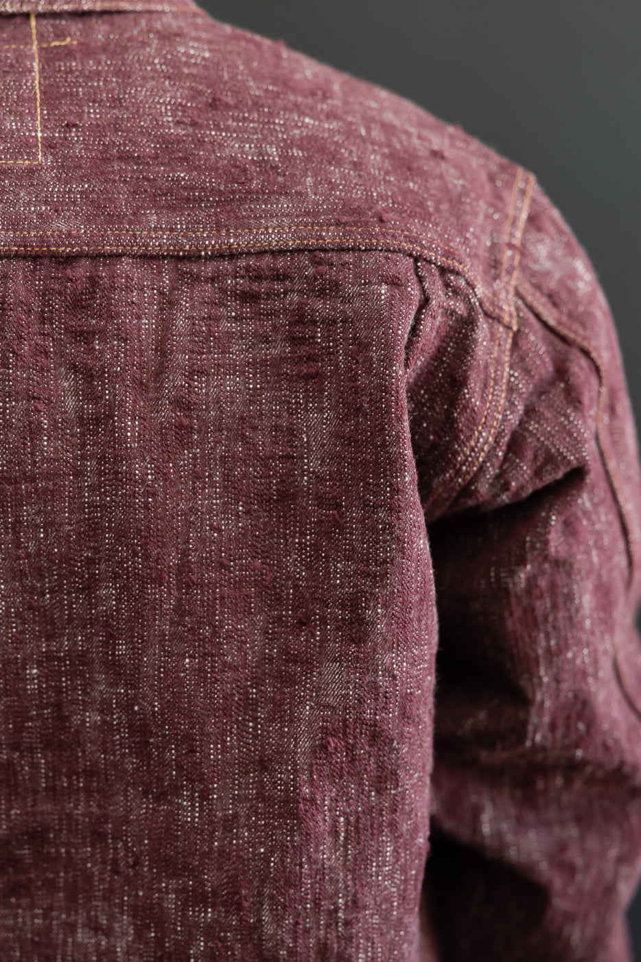 Close-up back view of burgundy selvedge shirt, showing shoulder seam & fabric texture on male model
