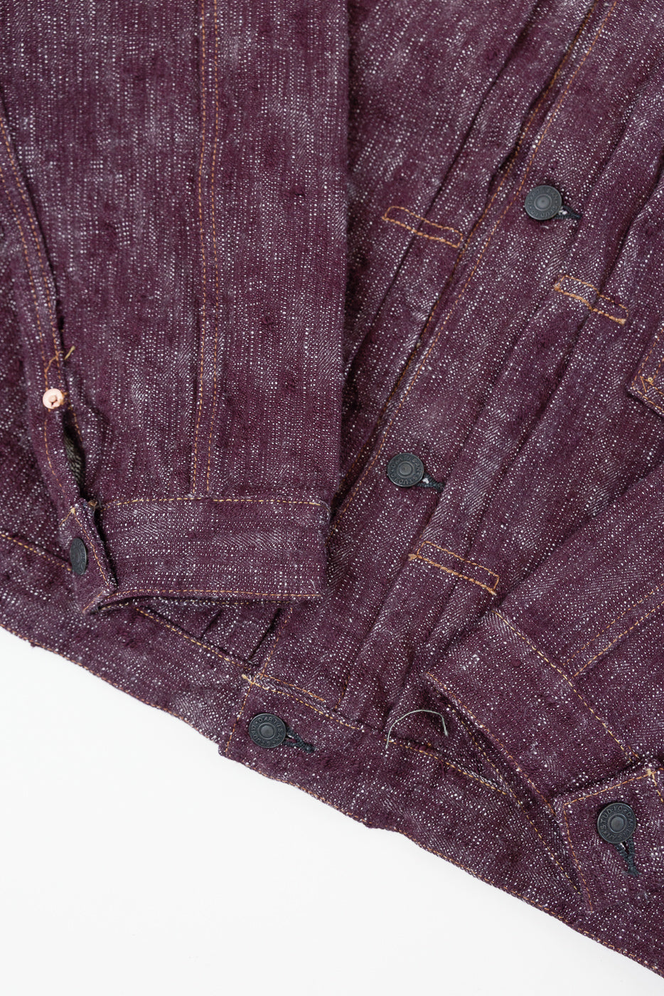Close-up front view of deep purple selvedge denim jacket with black buttons, orange stitching, and textured fabric weave