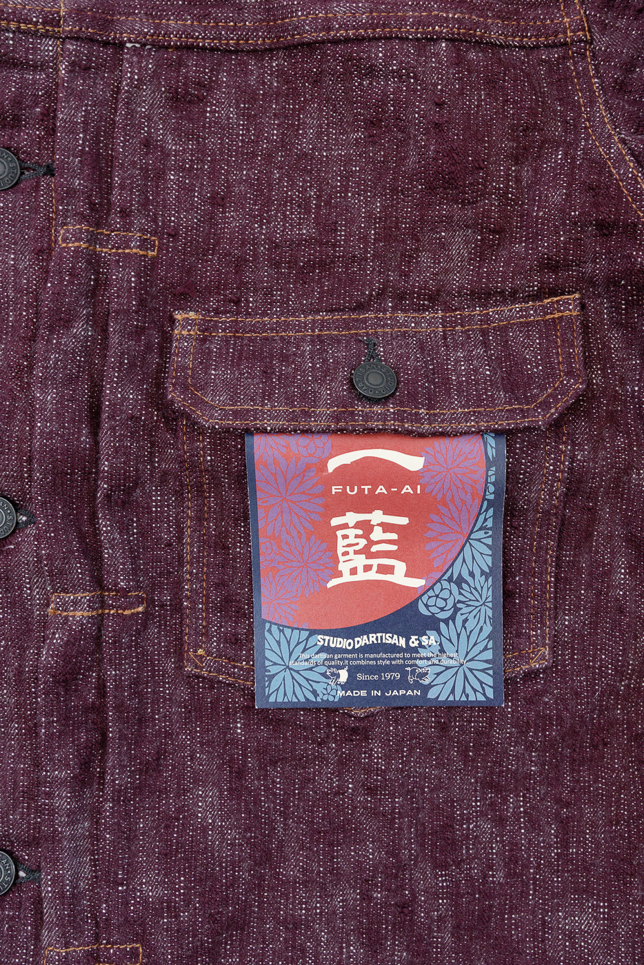 Close-up front view of burgundy selvedge shirt pocket with FUTA-AI tag, button, and orange stitching detail