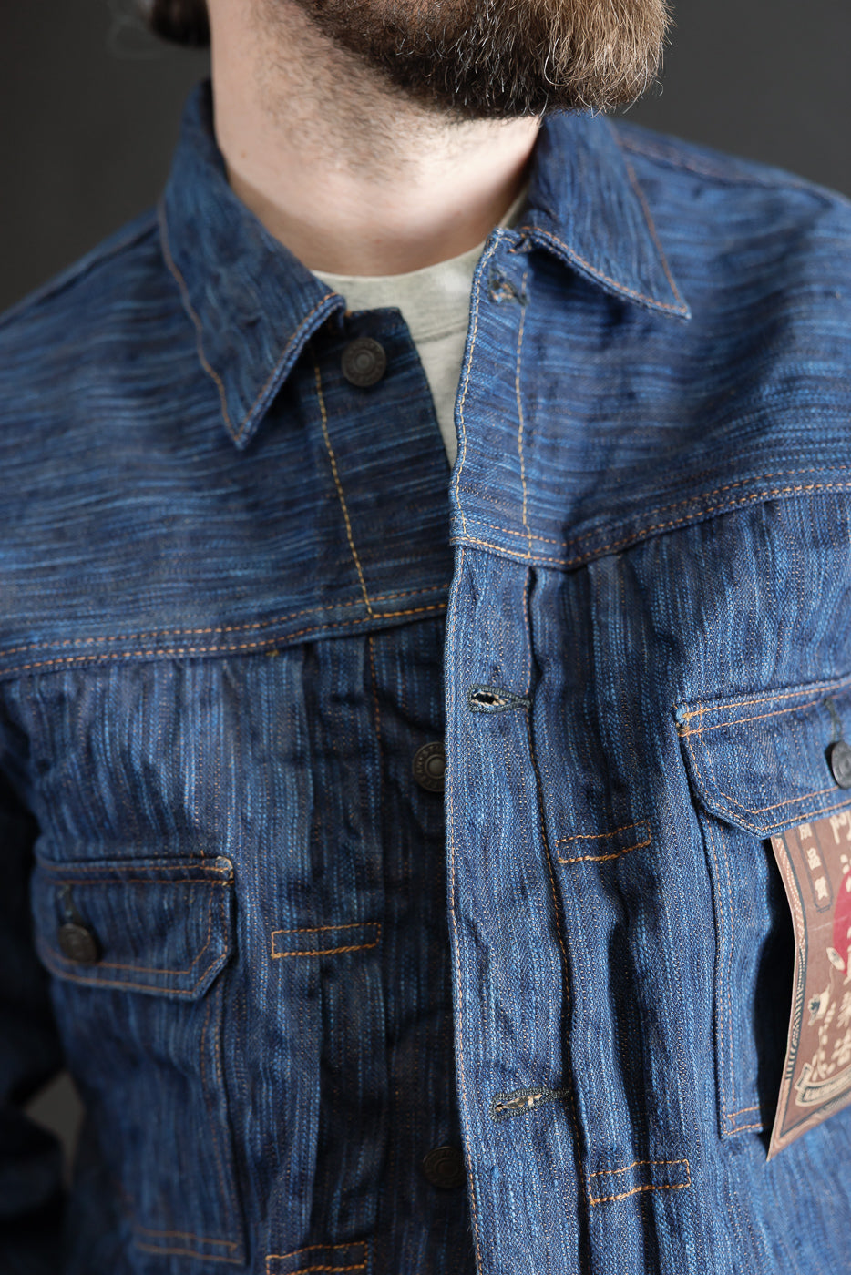 Close-up of front chest of men’s indigo selvedge denim jacket, showing collar, buttons, and pocket details, worn by a male model 5'9