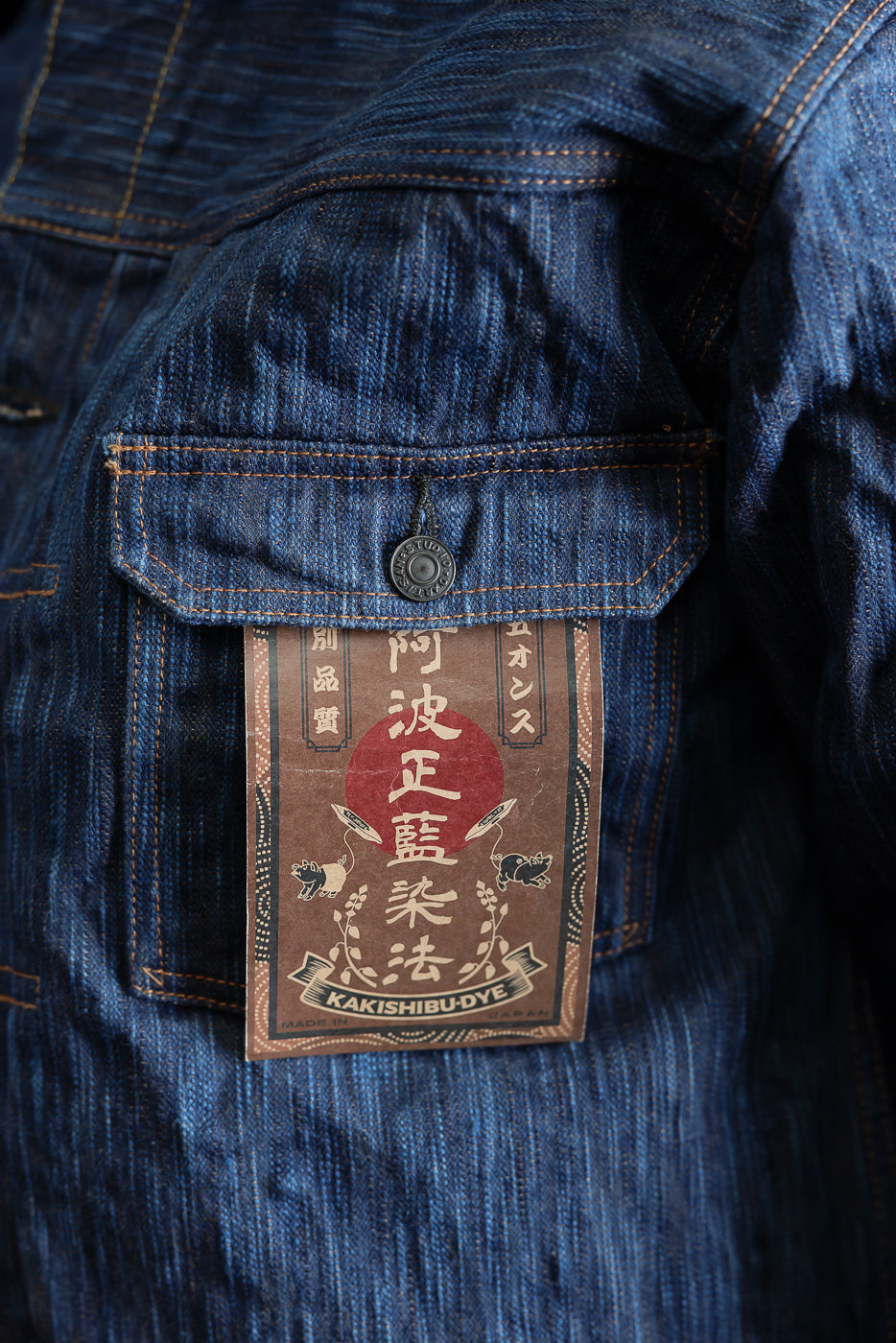 Close-up of front chest pocket and button on indigo selvedge denim jacket with Kakishibu tag