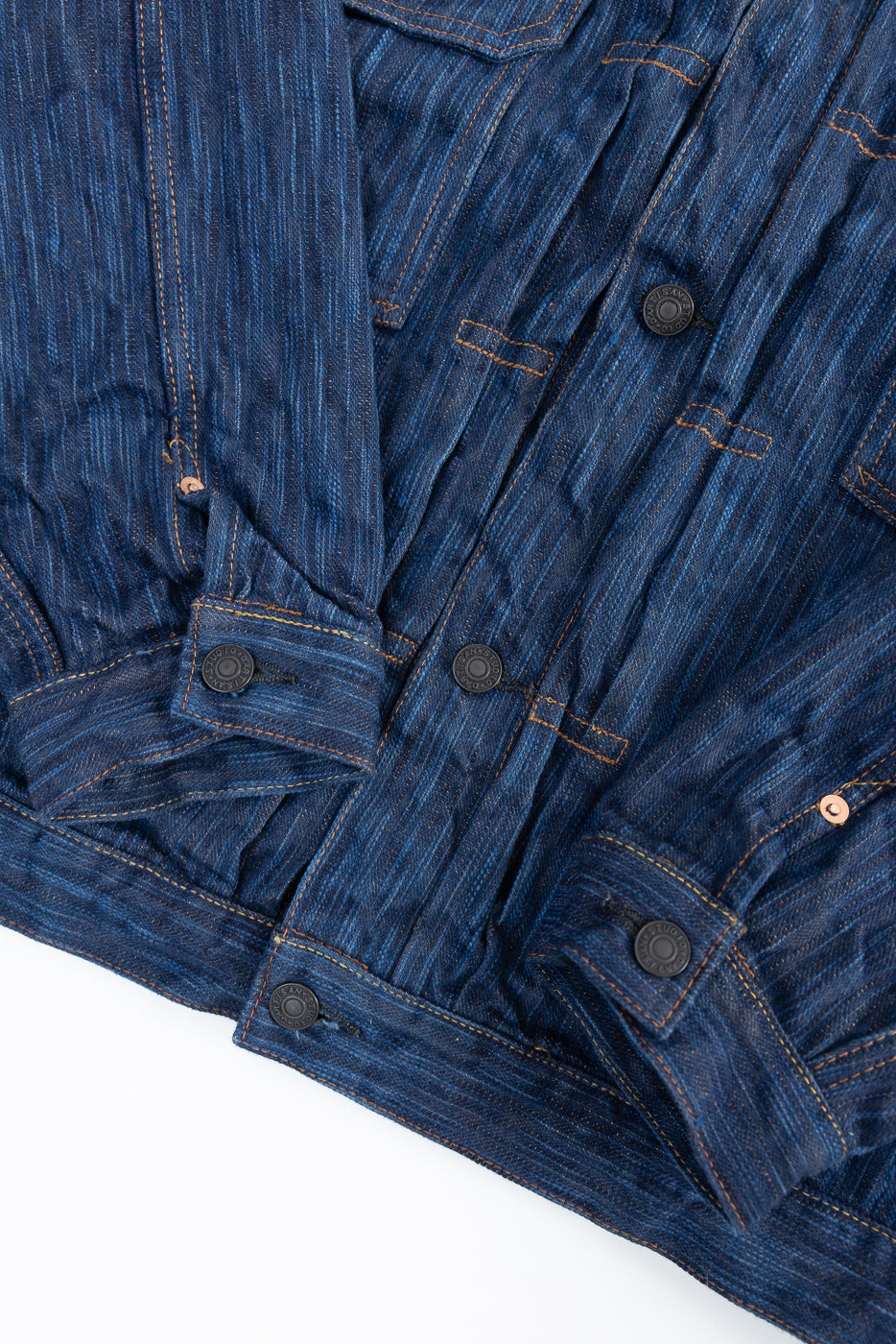 Close-up of front lower half of indigo selvedge denim jacket, showing button and hem details.