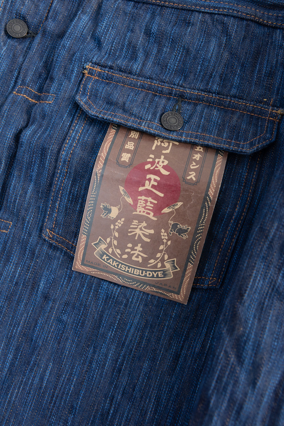 Close-up of front chest pocket and tag details on indigo selvedge jacket, showing texture and buttons.