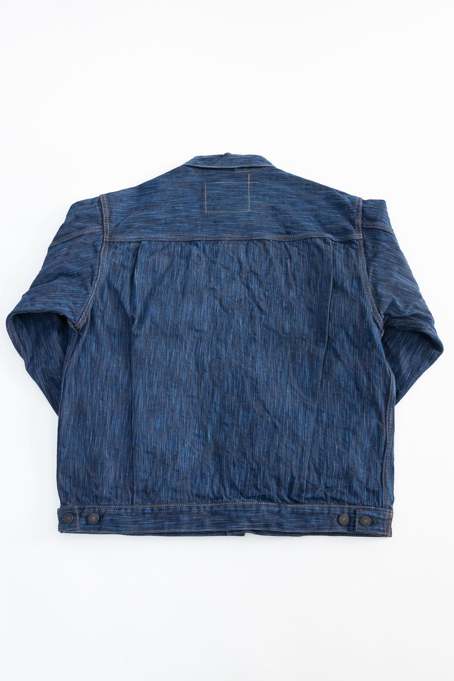 Flat lay of natural indigo selvedge denim jacket, back view, showing fabric texture and hem details.