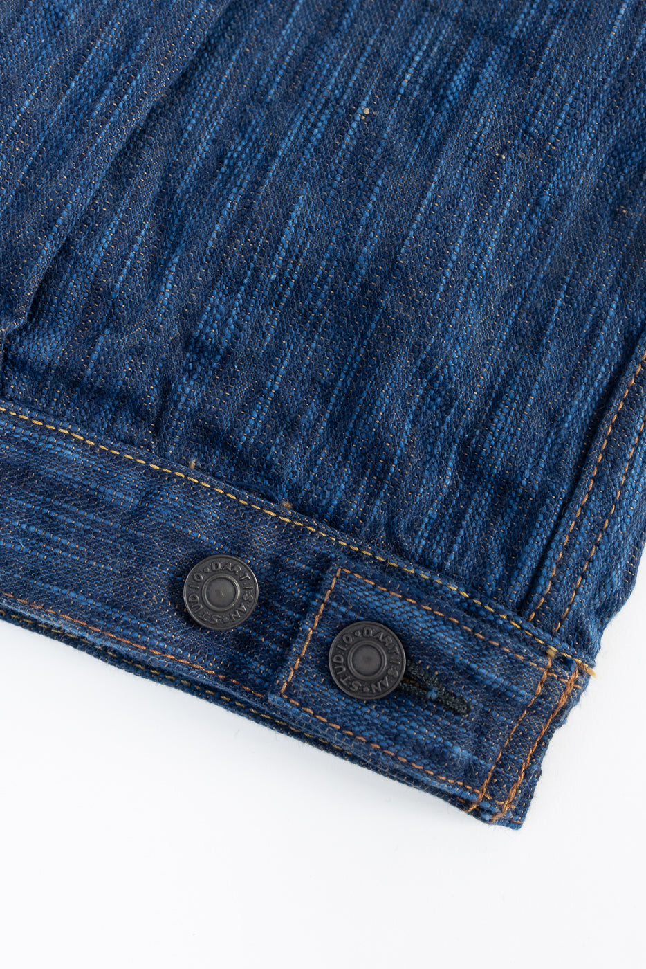 Close-up of jacket hem showing natural indigo selvedge denim texture and metal buttons.