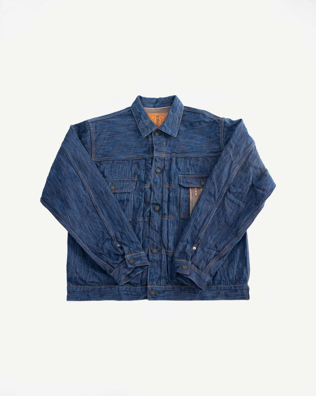 Flat lay of natural indigo selvedge denim jacket, front view showing chest pockets, buttons, and collar.