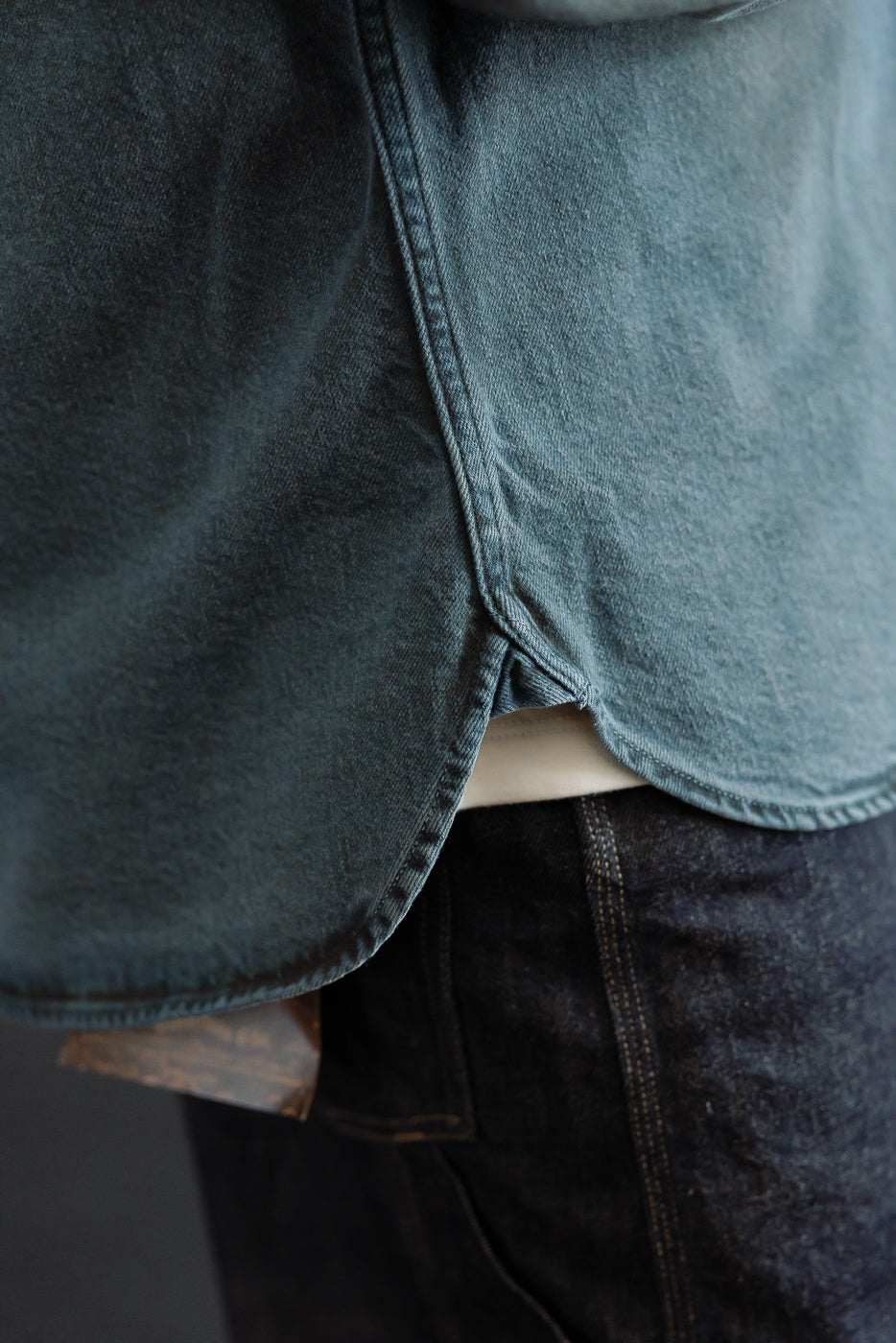 Close-up of the back hem of a blue denim jacket on a male model, 5'9