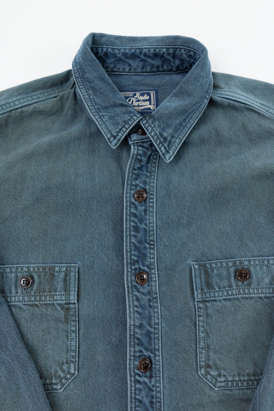 Close-up of the front of a blue Studio D'Artisan denim shirt showing the collar and tag.