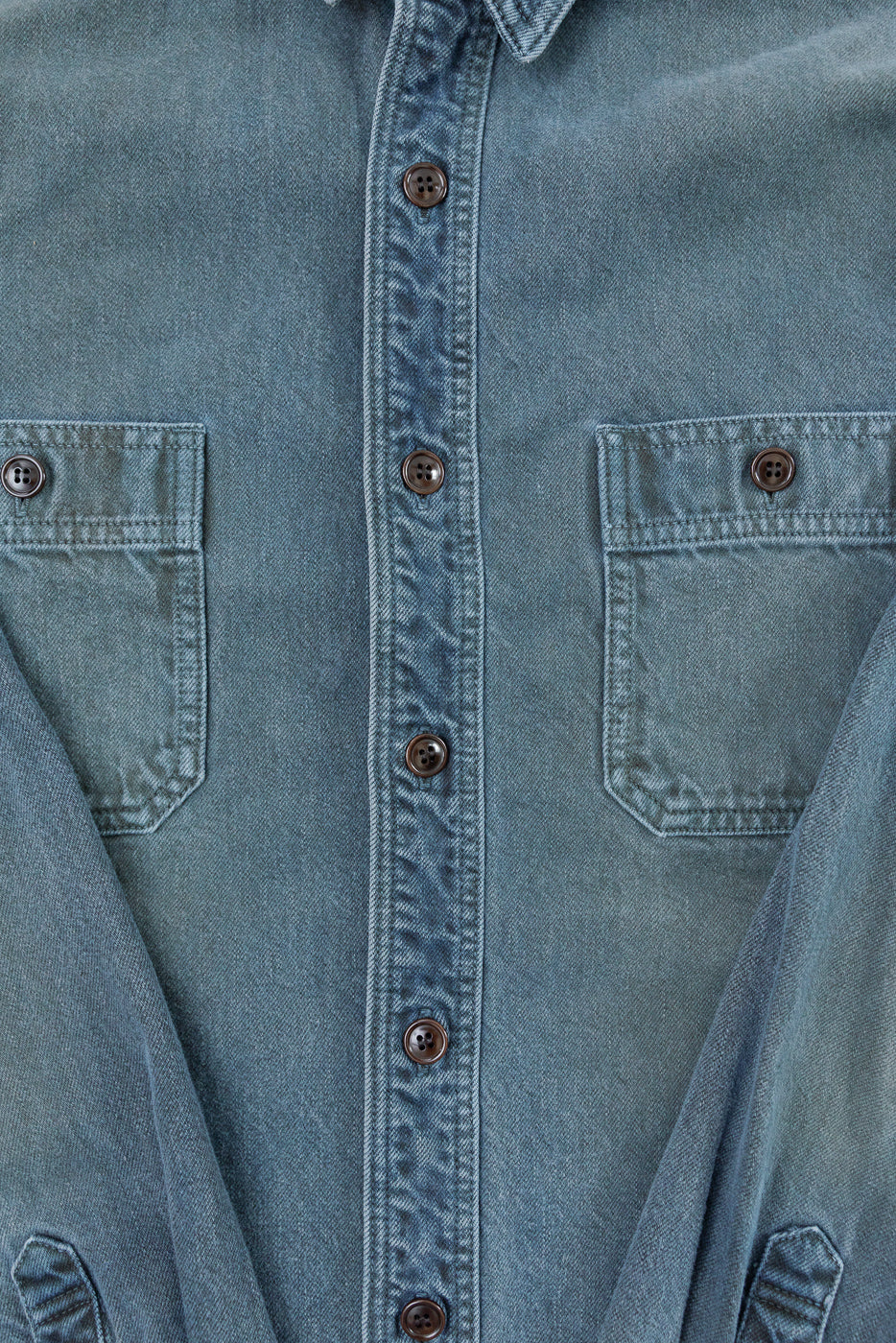 Close-up front view of a blue denim shirt showing buttons and chest pockets.
