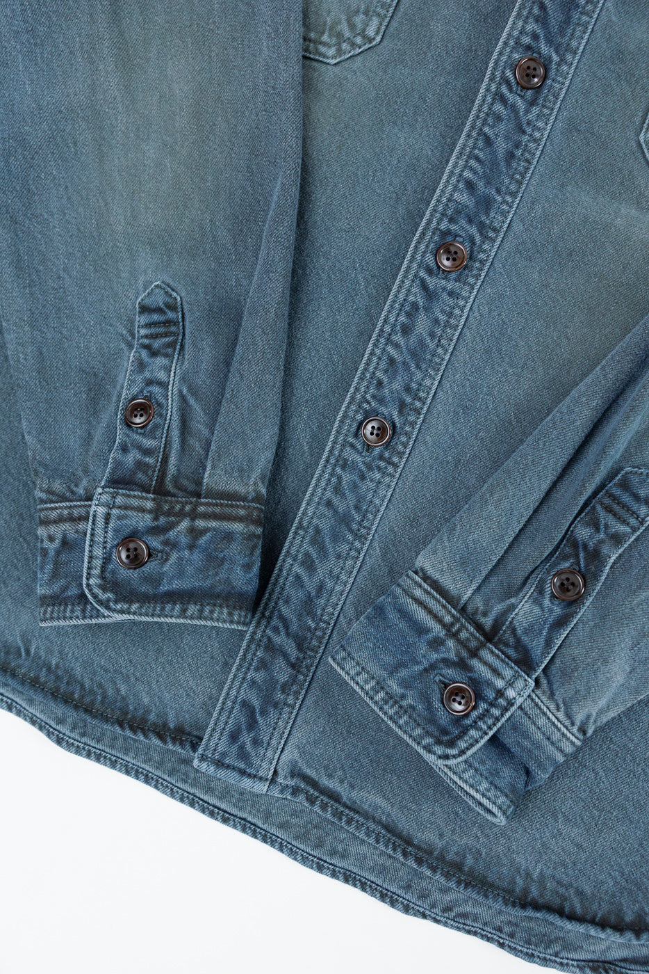 Close-up of the front right side of a blue denim shirt showing brown buttons and fabric texture.