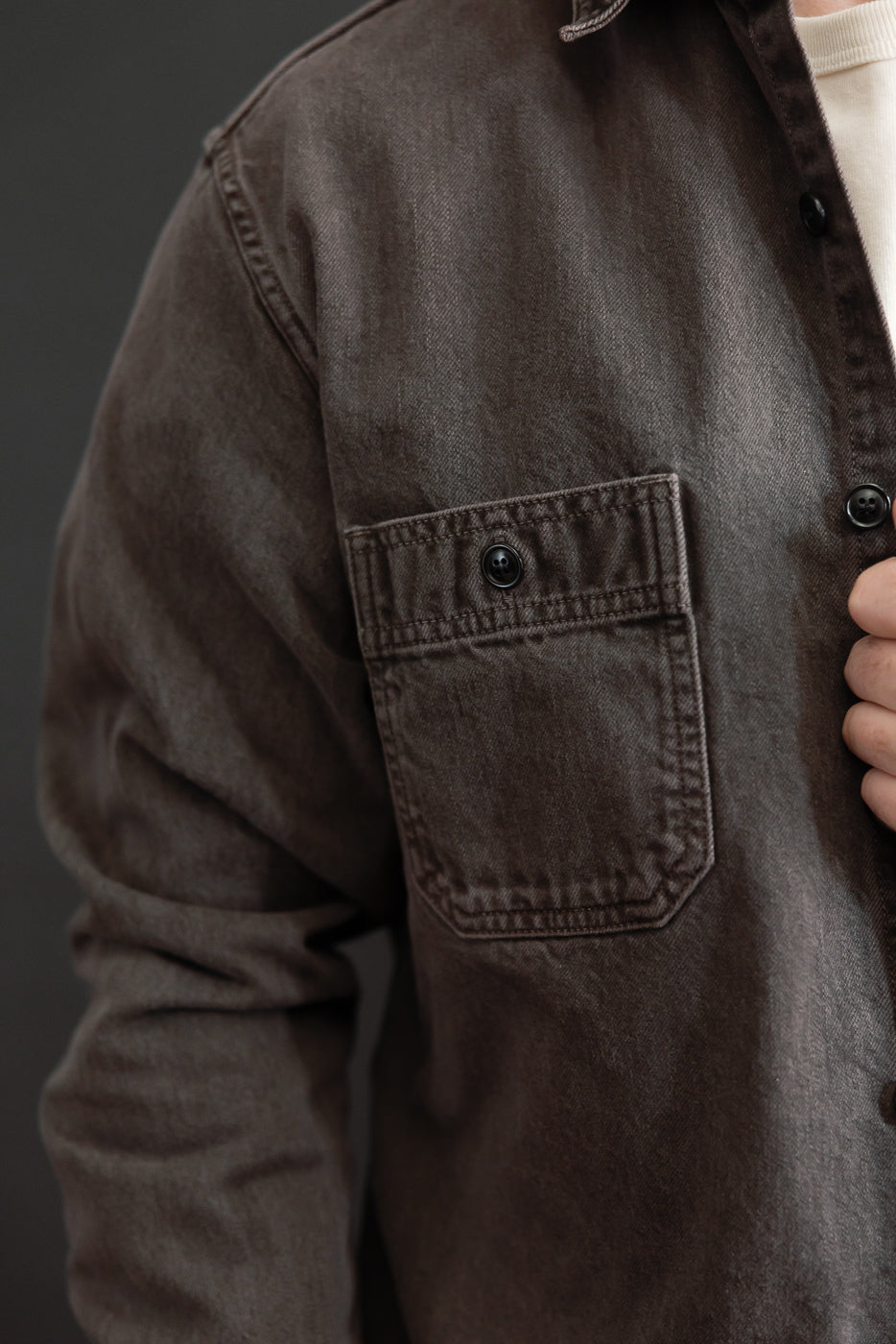 Close-up of the left chest pocket and button detail on a brown denim shirt.