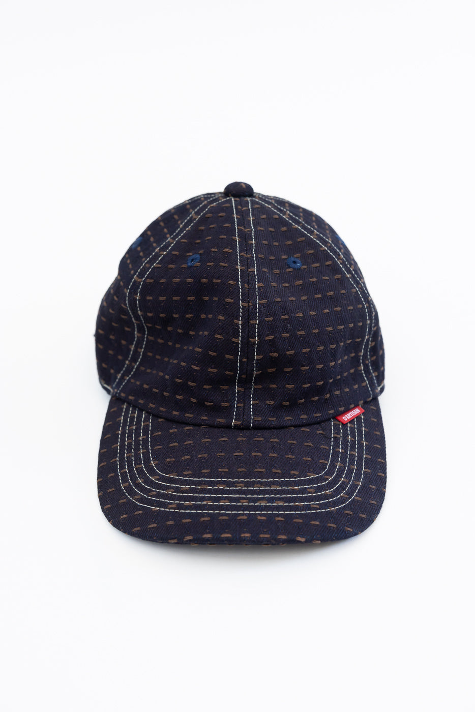 Front view of navy blue patterned baseball cap with white contrast stitching, red woven label, and structured brim.
