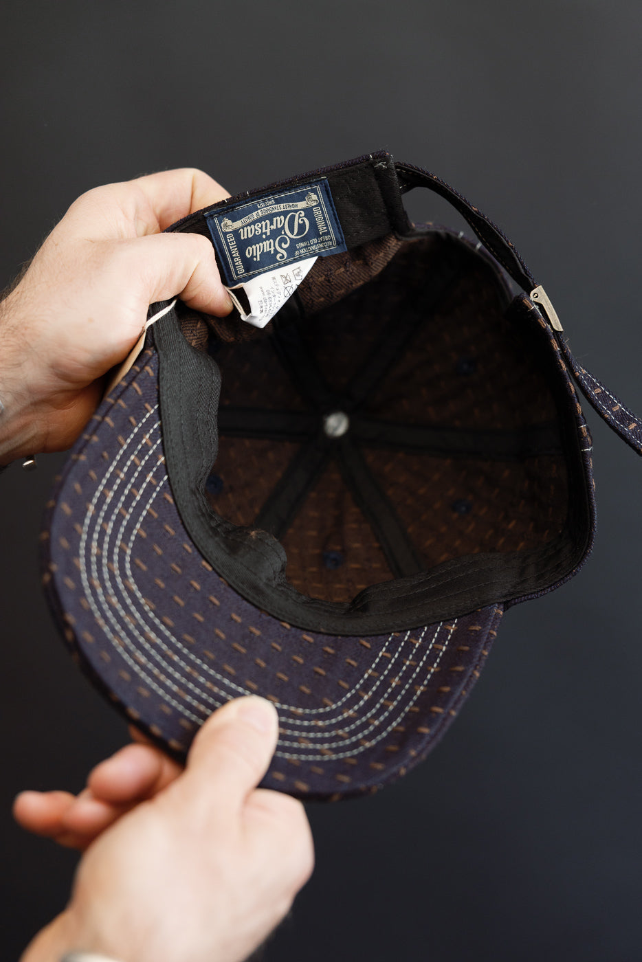 Close-up of cap's interior, showing tag and stitching details, held by hands