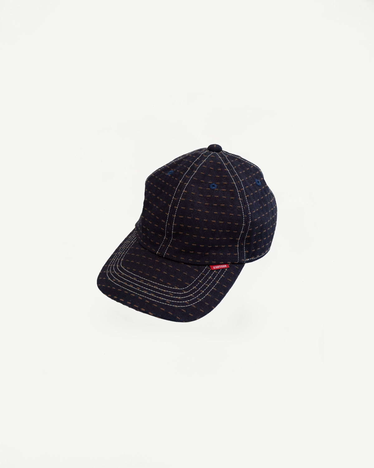 Dark navy baseball cap with tan stitch pattern, white contrast stitching, red brand tag, front view flat lay
