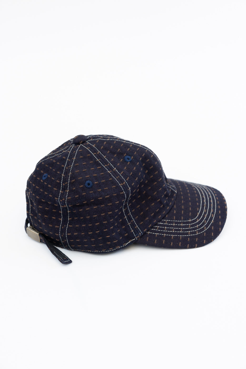 Navy blue patterned baseball cap, side view showing white stitching, adjustable strap, and fabric texture on white background.