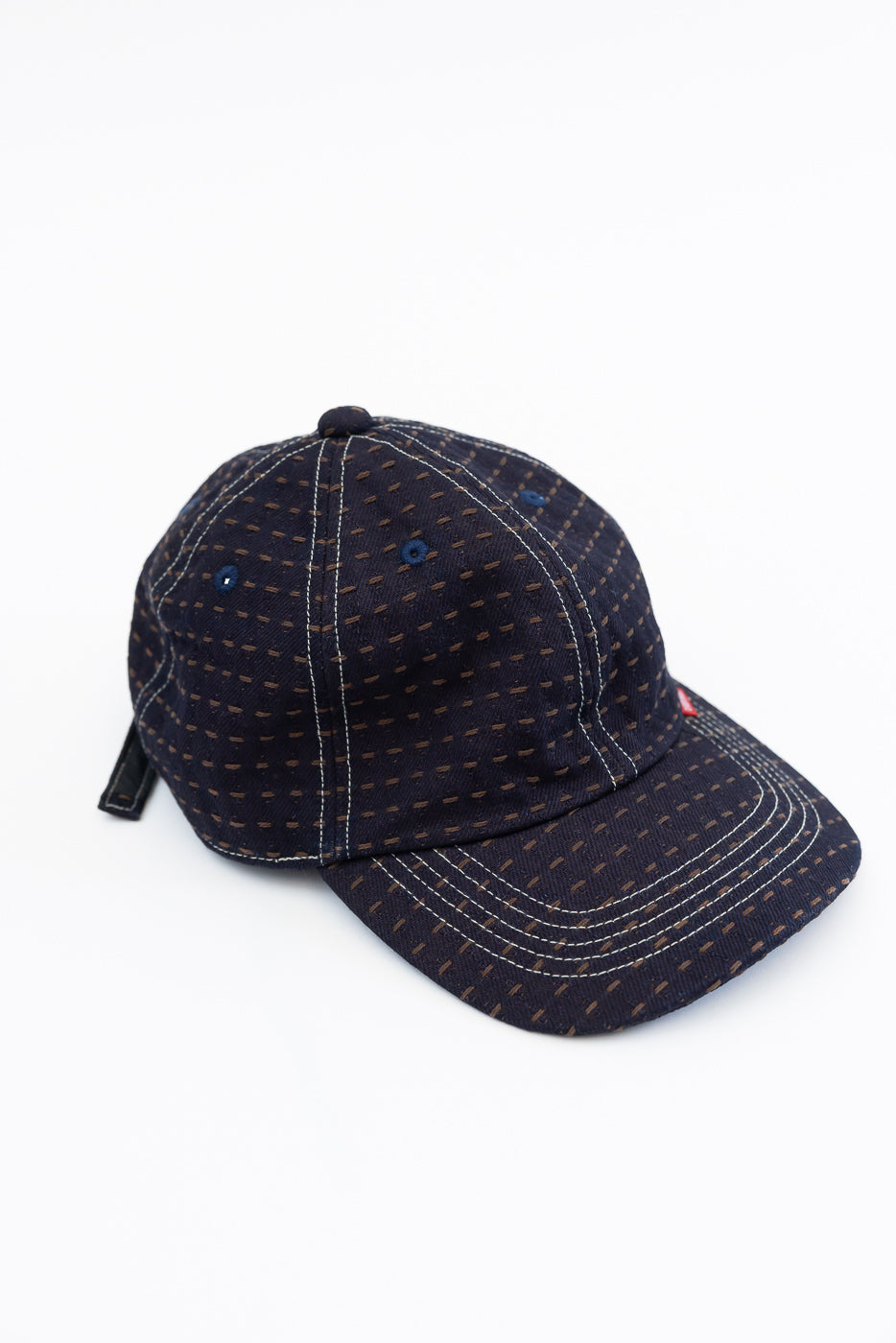 Dark navy baseball cap with subtle brown dash pattern, white contrast stitching, front view, flat lay