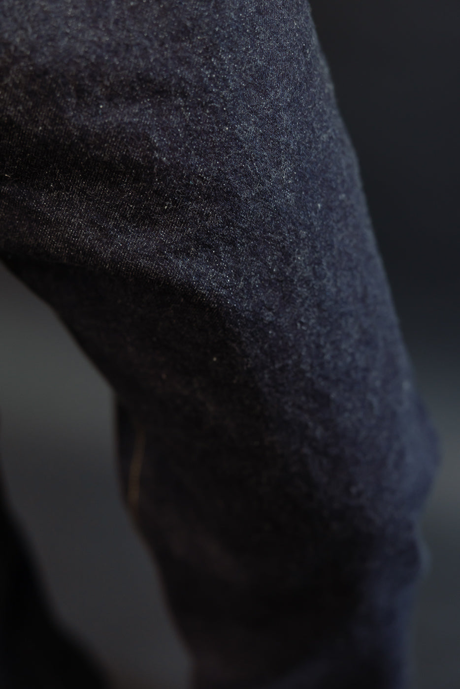 Close-up of dark selvedge denim fabric texture on male model's leg, showcasing weave detail and subtle fade