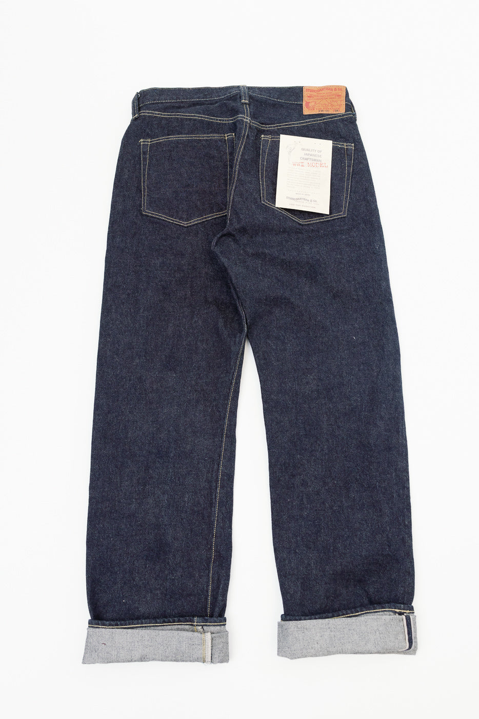 Back view flat lay of dark selvedge denim jeans, cuffed hems showing raw edge, back pocket tag details