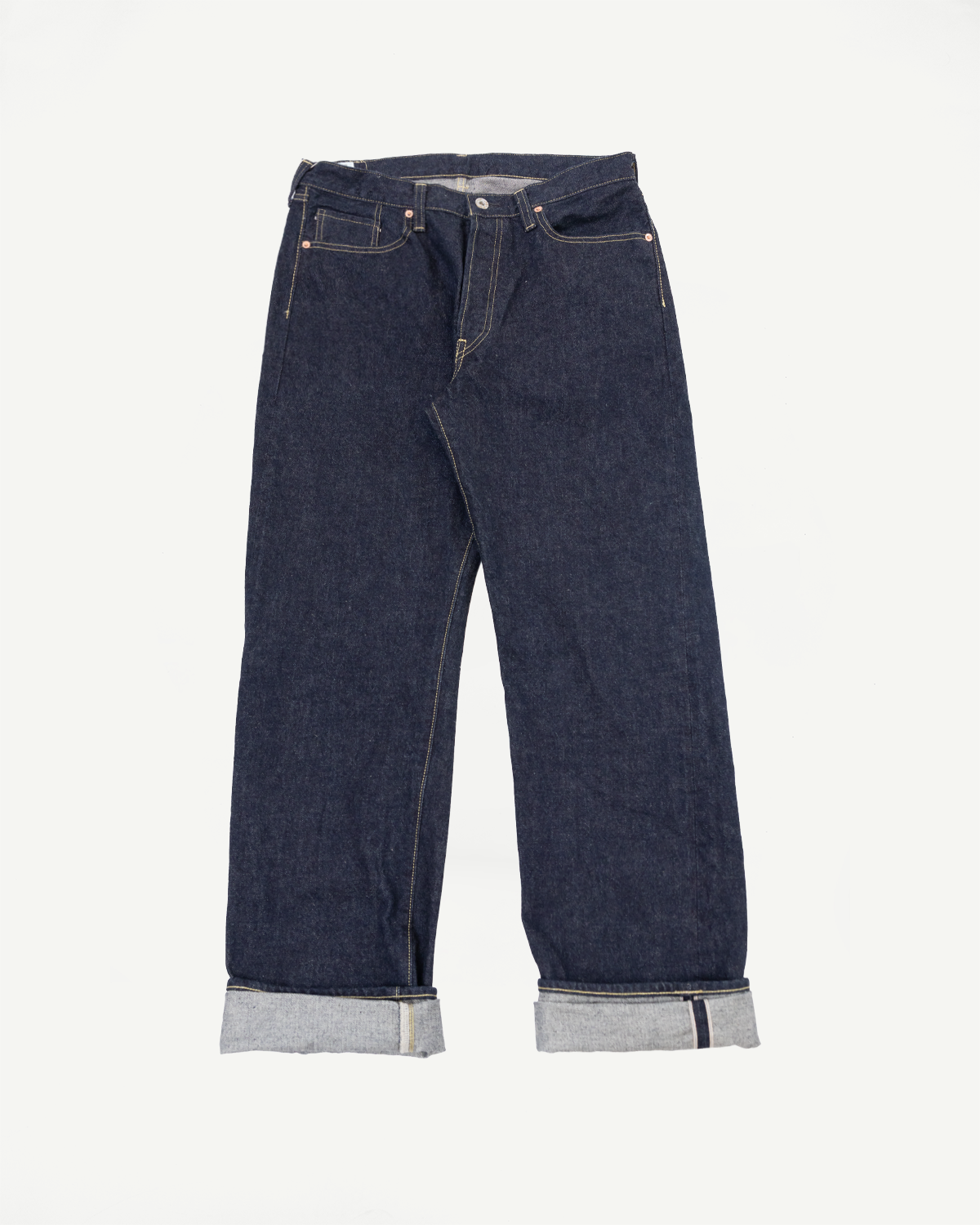 Front view flat lay of dark selvedge denim jeans with cuffed hems, visible stitching, and copper rivets