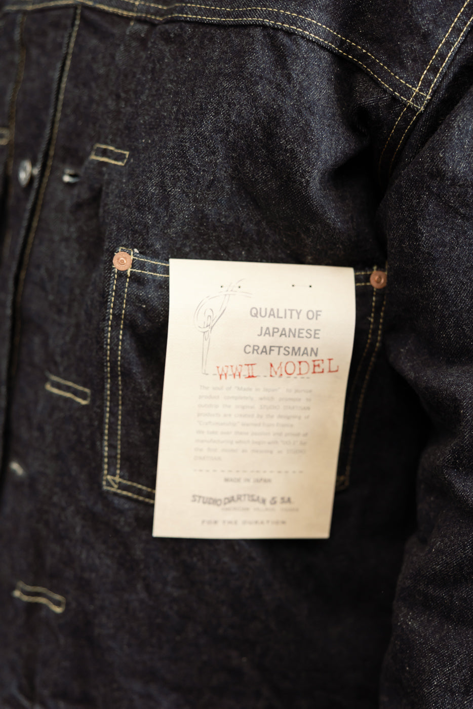 Close-up of dark selvedge denim jacket interior tag, showing 'WWII Model' and Japanese craftsmanship details