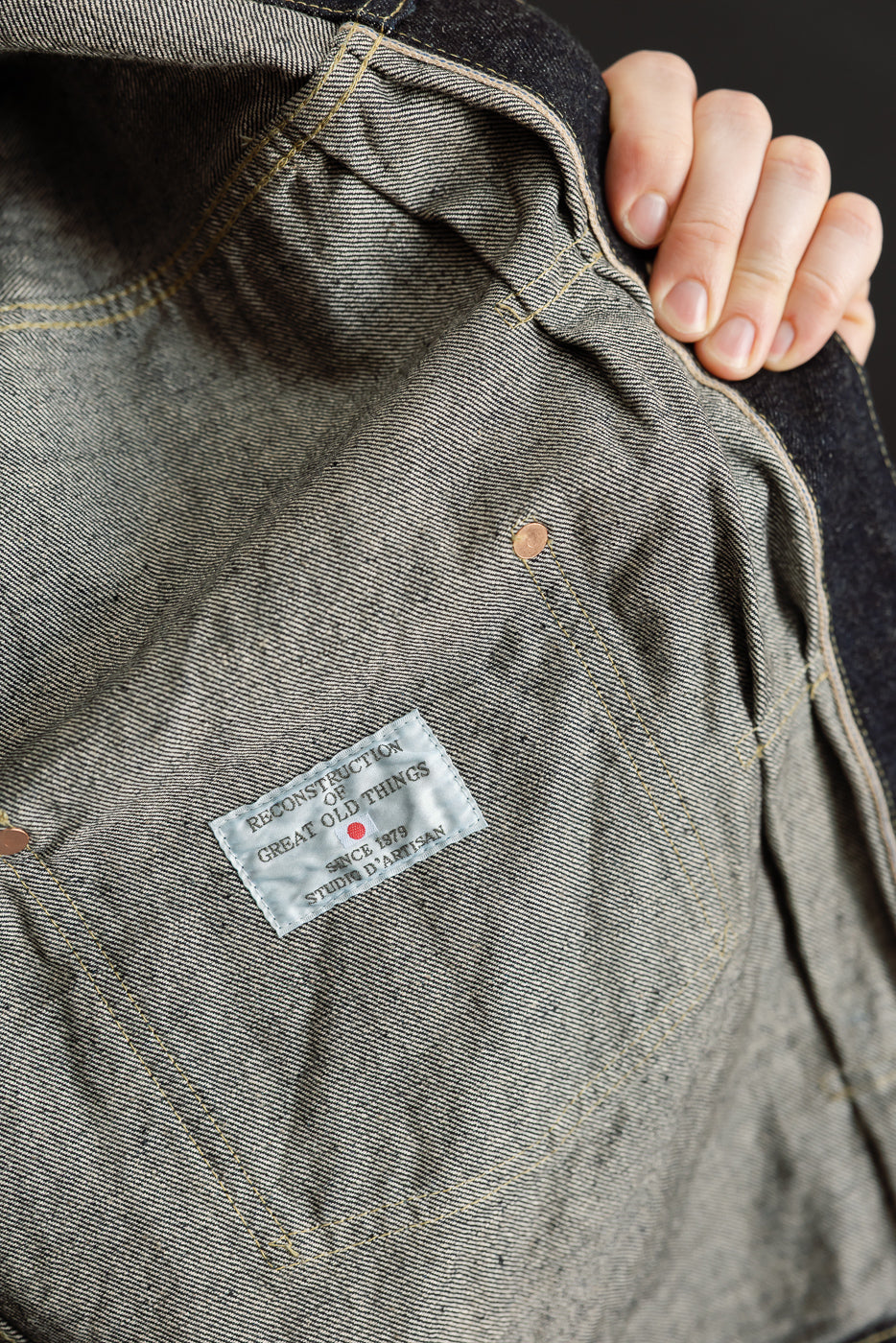 Close-up of selvedge denim jacket interior, showing brand label, copper rivets, and stitching detail