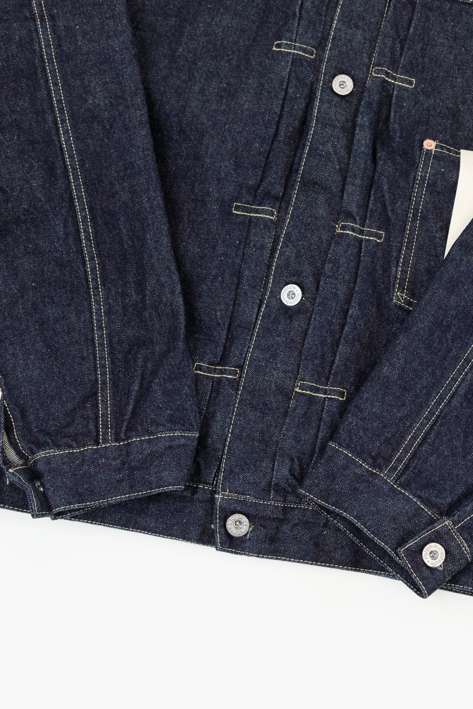 Close-up front view of dark selvedge denim jacket showing button placket, contrast stitching, and fabric texture