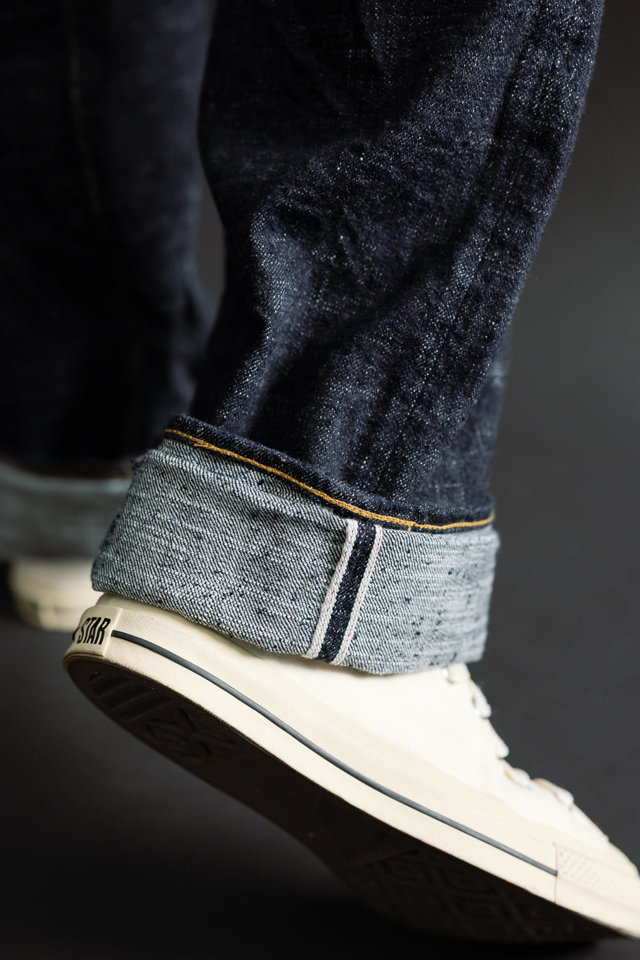 Close-up of male model’s lower legs in selvedge denim jeans, cuffed hem detail, side view.