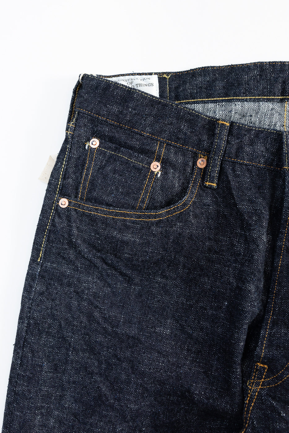 Close-up of front left side of dark indigo selvedge jeans showing pocket and rivet details.