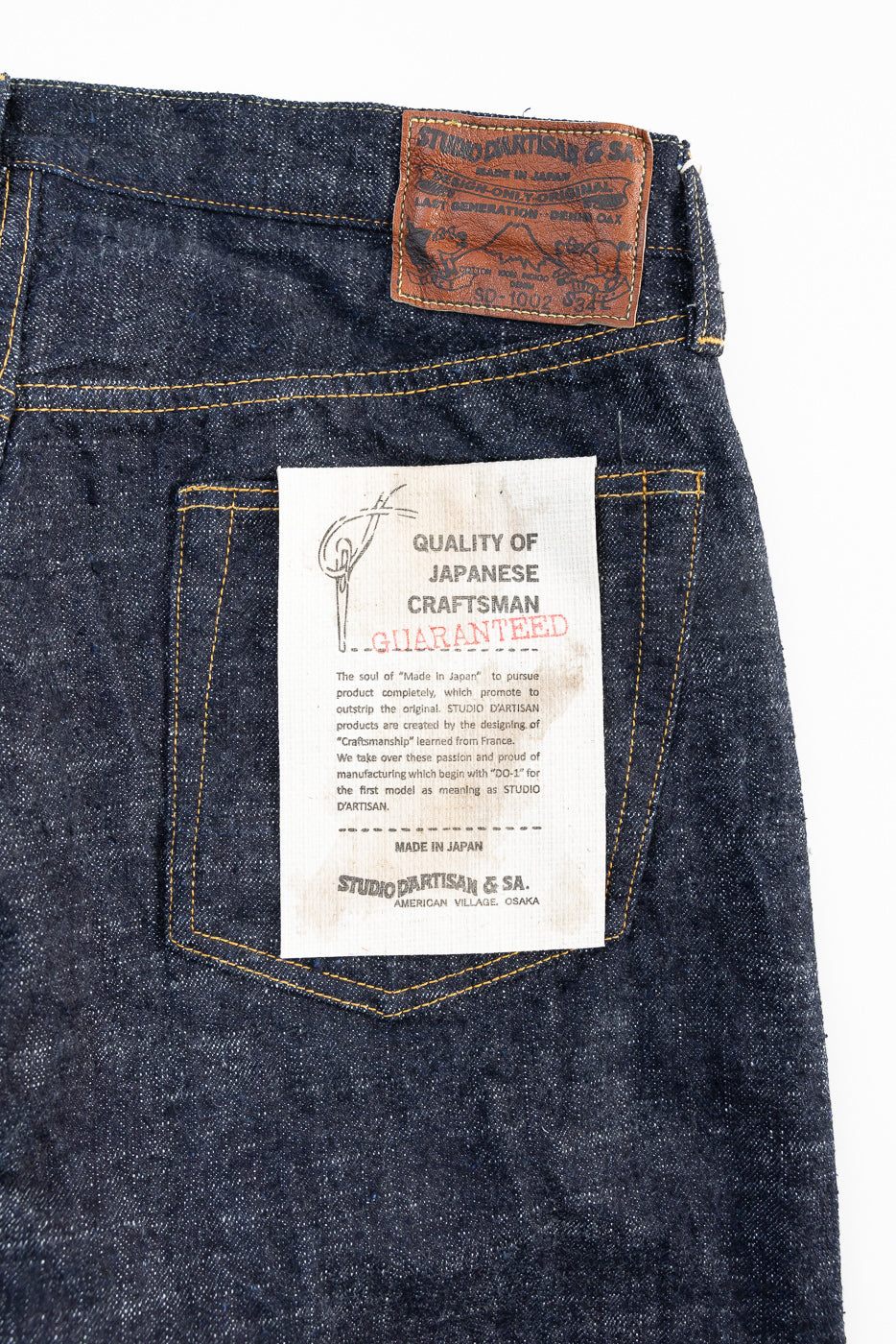 Close-up of the back side of selvedge jeans showing leather waist patch, pocket, and care tag details.