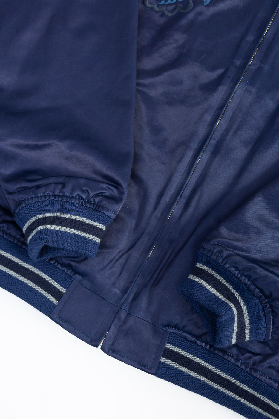 Close-up of indigo sukajan jacket front hem and striped ribbed cuffs detail.