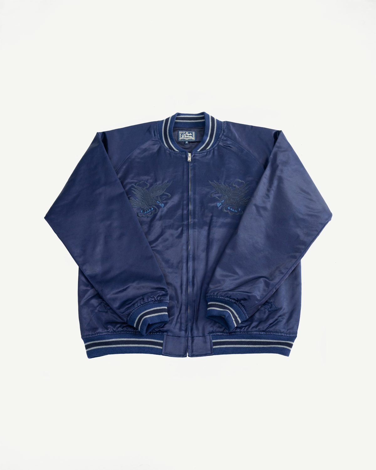 Flat lay of indigo-dyed sukajan jacket, front view, showing embroidery and striped trim details.