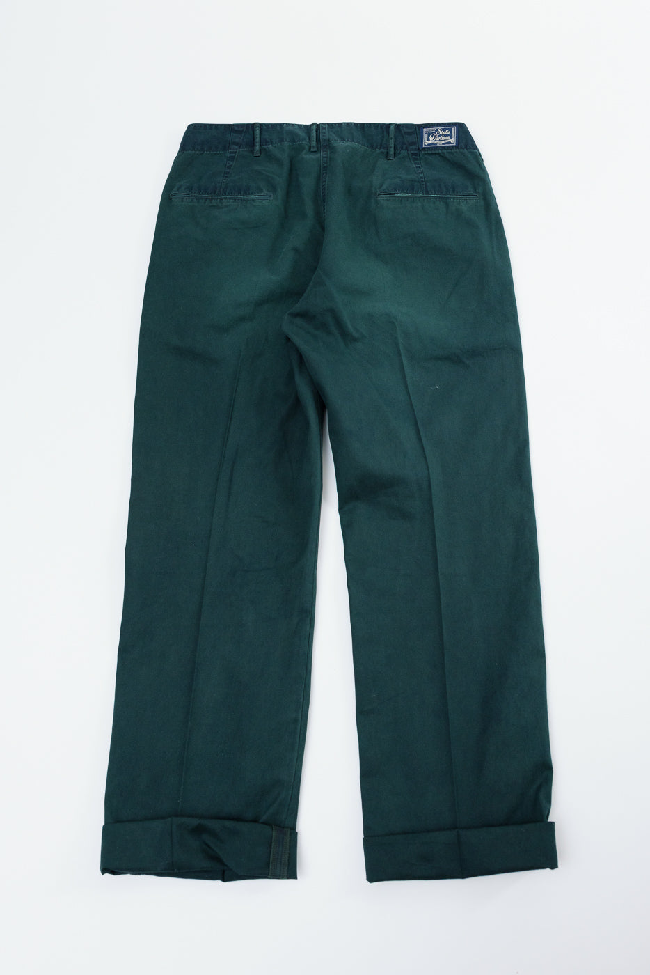 Back view flat lay of dark green chinos with cuffed hems and brand patch on waistband
