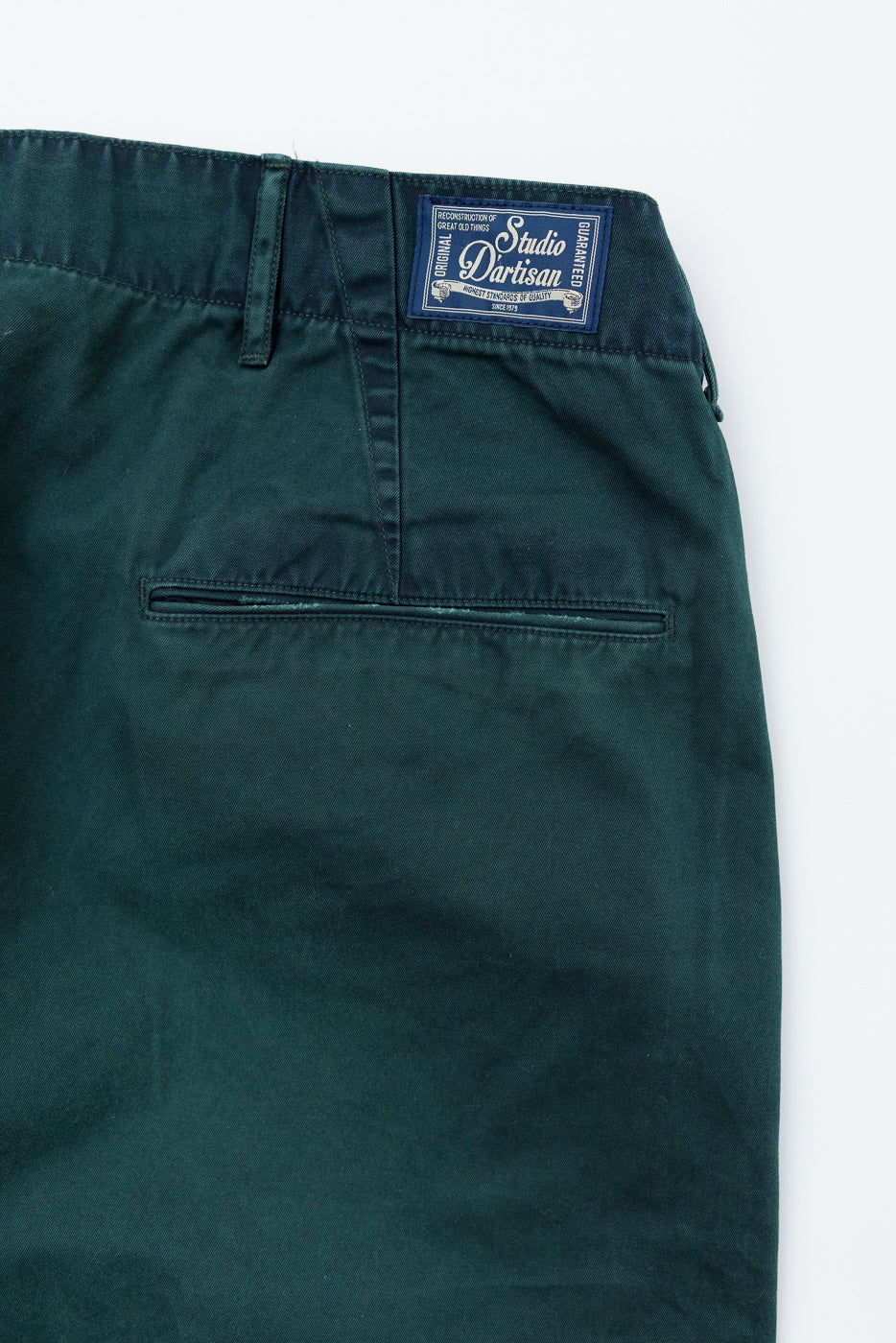 Close-up back view of dark green chinos showing Studio D'artisan waistband label and rear pocket detail