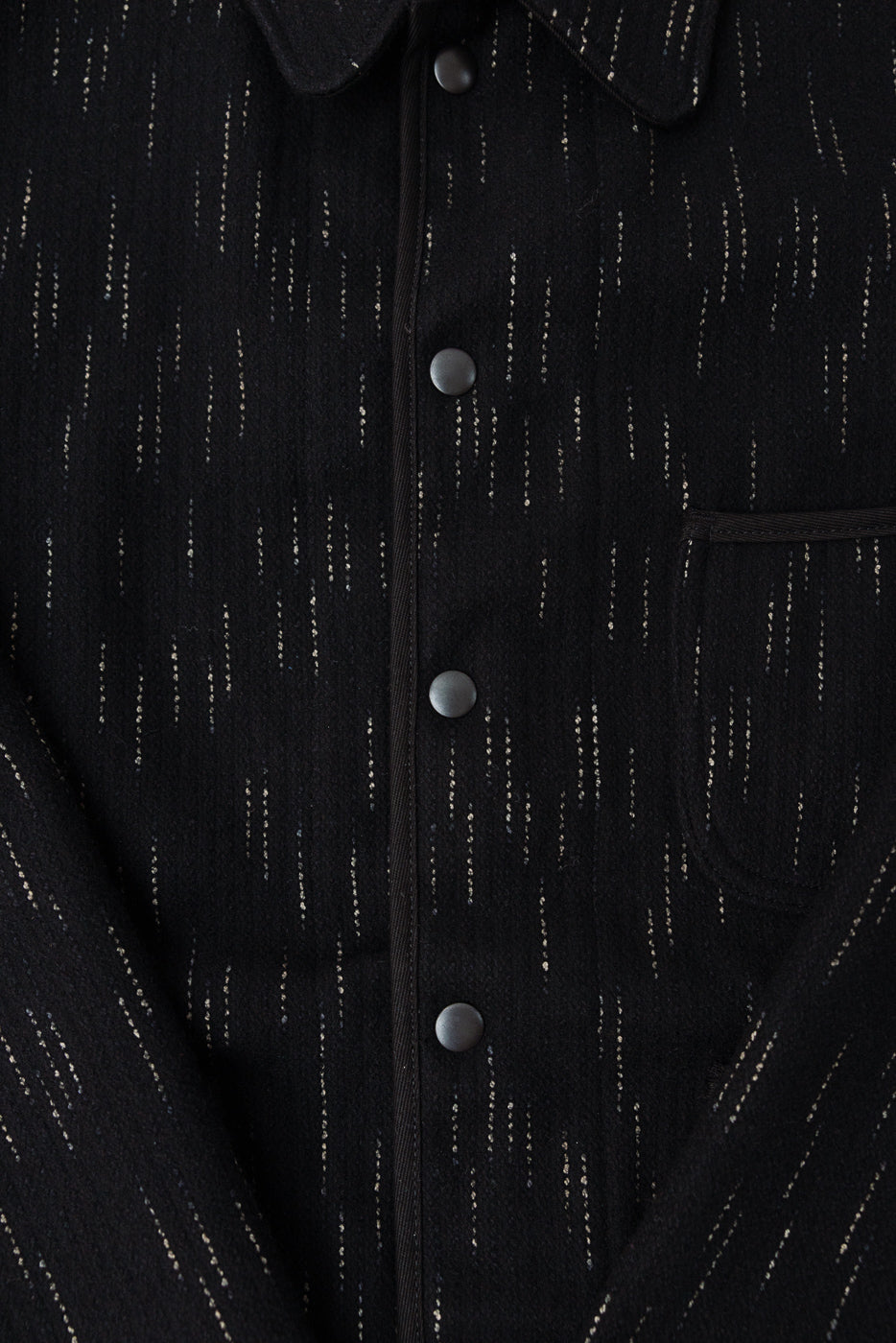 Close-up front detail of Studio D’Artisan black kasuri-dyed beach cloth coverall, snap buttons, chest pocket, textured fabric.