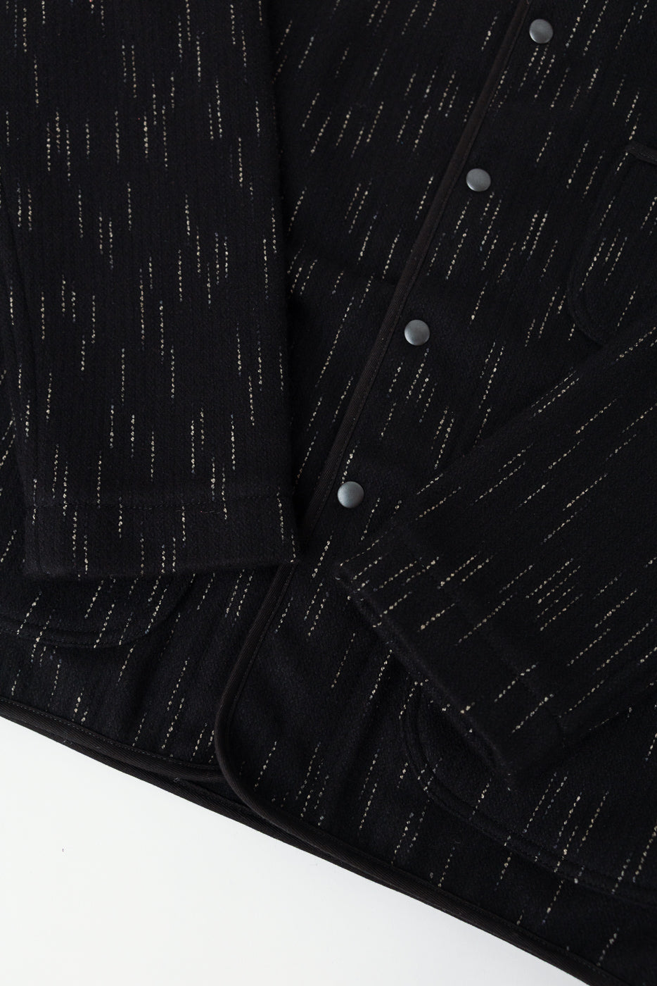 Close-up of black kasuri-dyed beach cloth coverall front, highlighting snap buttons, fabric texture, and sleeve cuff details.