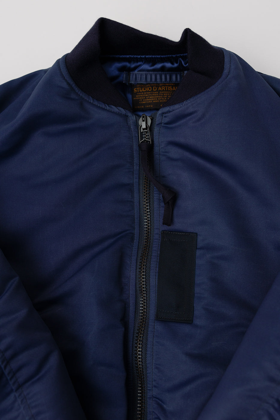 Close-up front detail of Studio D’Artisan indigo MA-1 flight jacket, zipper, ribbed collar, fabric texture.