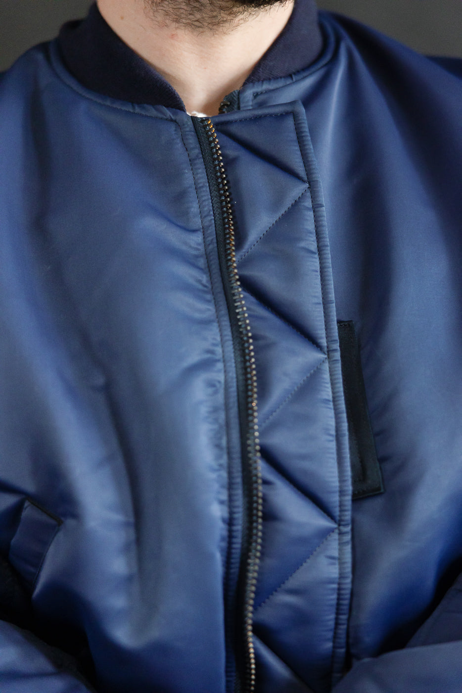 Close-up front of indigo MA-1 flight jacket on male model, showing zipper and quilted texture