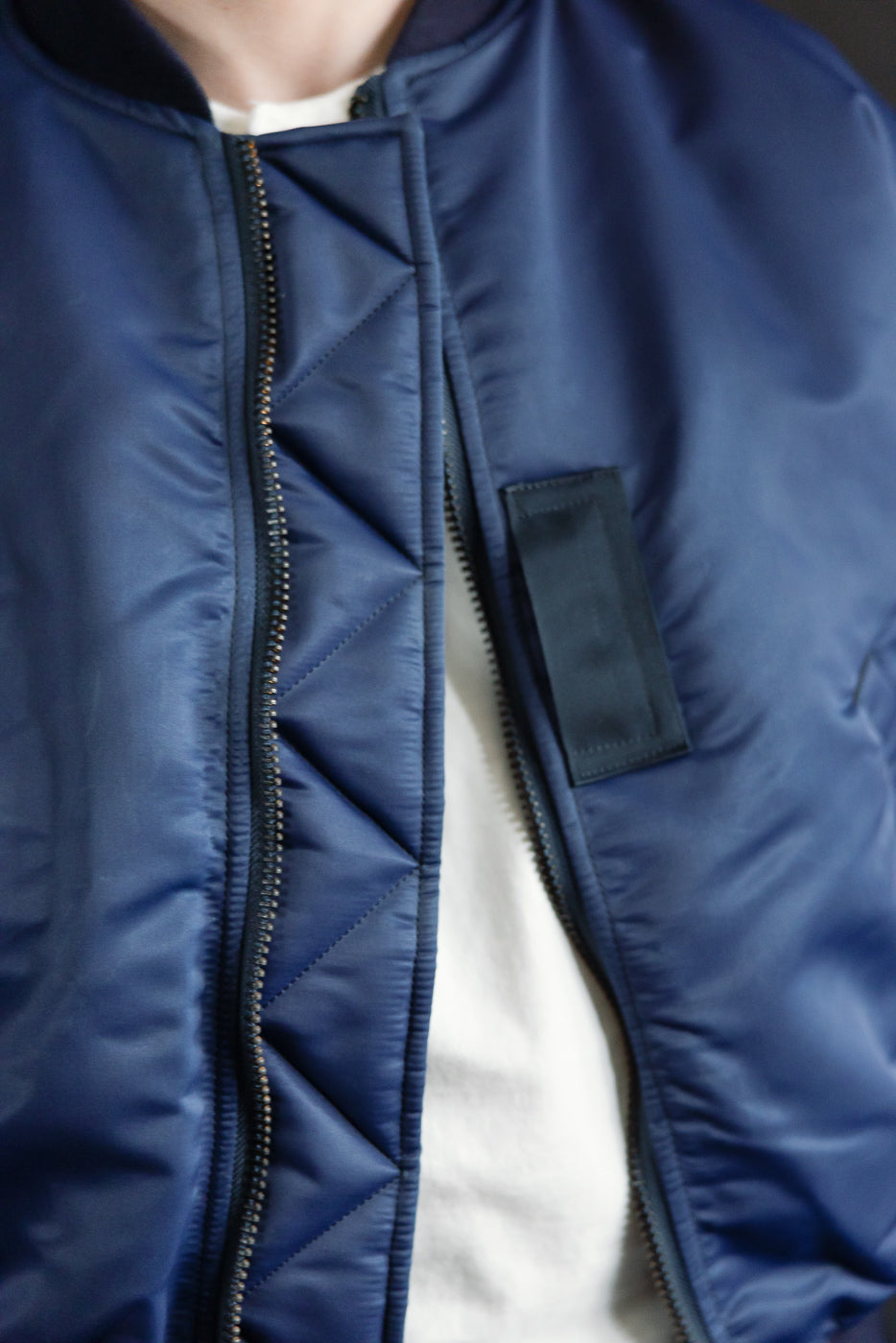 Close-up front view of indigo MA-1 flight jacket on male model, showing zipper and fabric texture