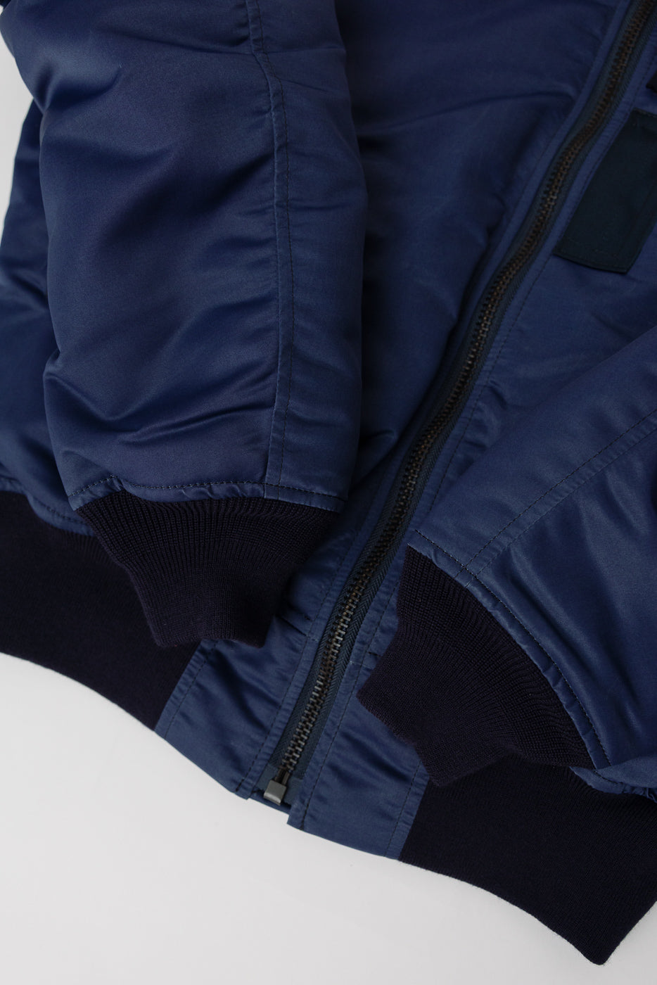 Close-up of Studio D'Artisan MA-1 indigo flight jacket front, showing ribbed cuffs and zipper.