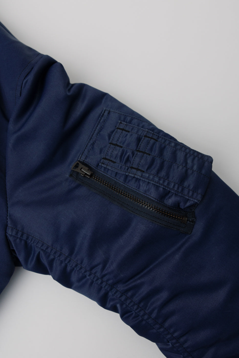Close-up of indigo MA-1 flight jacket sleeve pocket, visible zipper and stitching details