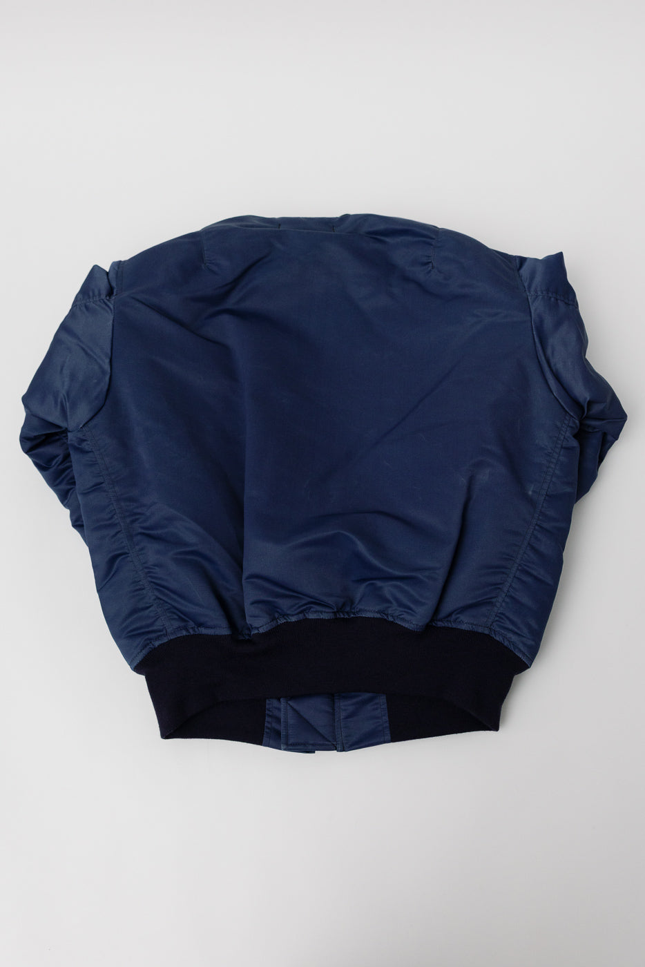 Studio D’Artisan indigo MA-1 flight jacket back flat lay, showing ribbed hem and fabric texture