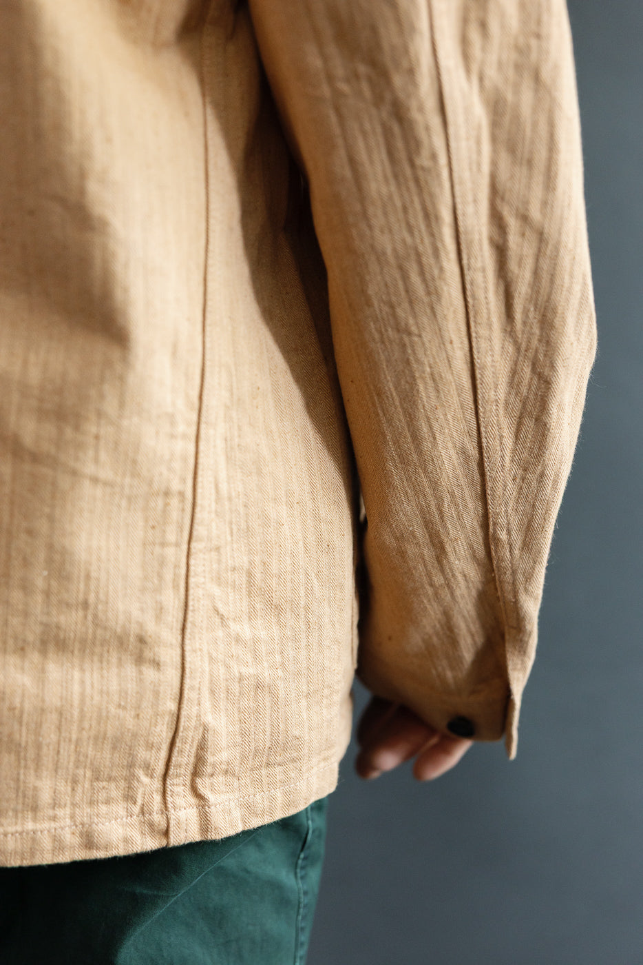 Close-up of male model's side, showcasing tan shirt's textured fabric, sleeve, and button detail.