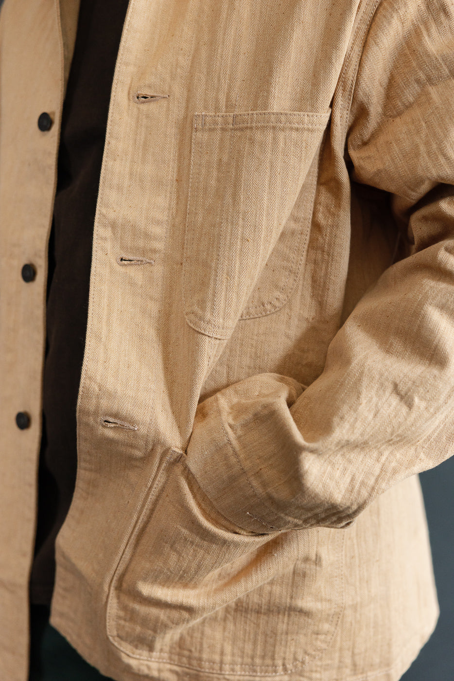 Close-up of male model's left side showing tan herringbone shirt with chest pocket, button placket, and sleeve detail