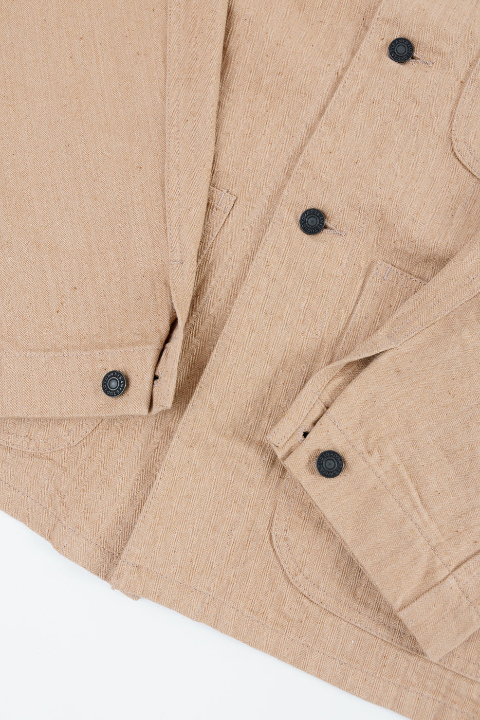 Close-up front view of tan herringbone jacket with black buttons, chest pockets, and textured fabric detail